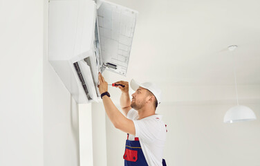 Worker installing a new modern air conditioning system. Young man in a uniform cap installing an air conditioner on a white wall in the house. AC installation, maintenance, repair service concept