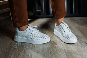 Slender female legs in pants close-up in white casual sneakers. Women's leather shoes.