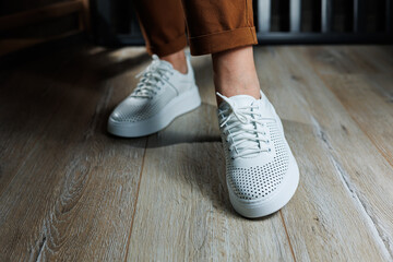 Slender female legs in pants close-up in white casual sneakers. Women's leather shoes.