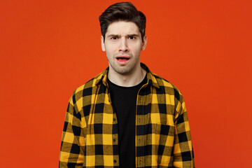 Young sad dissatisfied displeased caucasian man wear yellow checkered shirt black t-shirt looking camera with opened mouth isolated on plain red orange background studio portrait. Lifestyle concept.