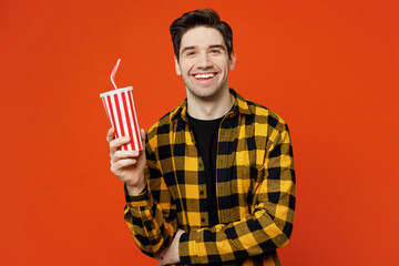 Young caucasian man he wear yellow checkered shirt black t-shirt hold in hands cup of soda pop cola fizzy water look camera isolated on plain red orange background studio portrait. Lifestyle concept. - obrazy, fototapety, plakaty