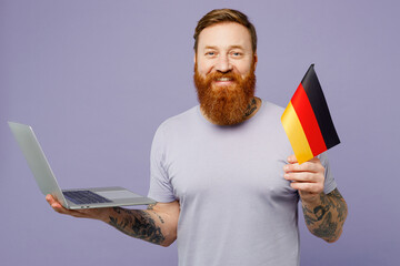 Young redhead bearded IT man he wear violet t-shirt casual clothes hold german flag use work on...