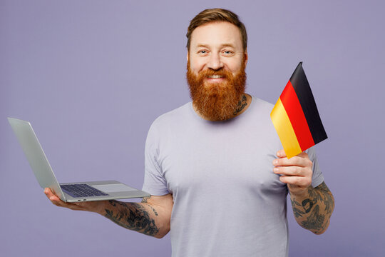 Young redhead bearded IT man he wear violet t-shirt casual clothes hold german flag use work on laptop pc computer isolated on plain pastel light purple background studio portrait. Lifestyle concept.
