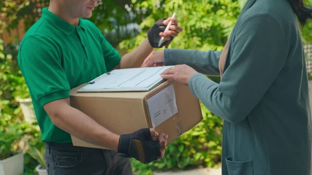 Cropped shot of delivery man in green T-shirt giving receipt to sign and box to female client outdoors