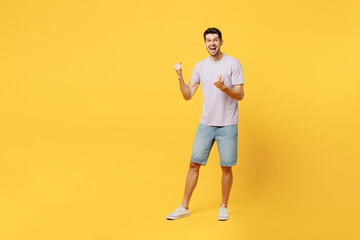 Fototapeta na wymiar Full body excited side view young man he wear light purple t-shirt casual clothes doing winner gesture celebrate clenching fists say yes isolated on plain yellow background studio. Lifestyle concept.