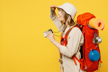 Side view young woman carry backpack with stuff mat use binocular look aside isolated on plain yellow background Tourist leads active lifestyle walk on spare time Hiking trek rest travel trip concept