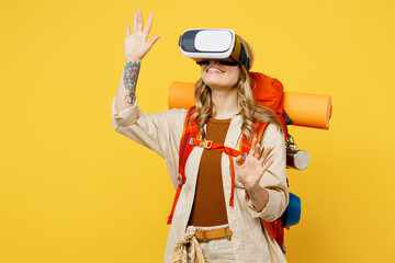 Young woman carry backpack with stuff mat watching in vr headset pc gadget isolated on plain yellow background. Tourist leads active lifestyle walk on spare time. Hiking trek rest travel trip concept