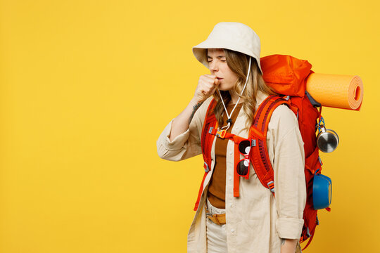 Side View Young Sick Woman Carry Backpack With Stuff Mat Cough Cover Mouth Isolated On Plain Yellow Background. Tourist Leads Active Lifestyle Walk On Spare Time. Hiking Trek Rest Travel Trip Concept.