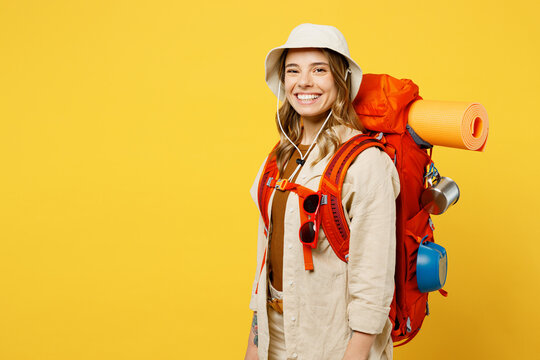 Side View Happy Young Woman Carrying Backpack With Stuff Mat Look Camera Isolated On Plain Yellow Background. Tourist Leads Active Lifestyle Walk On Spare Time. Hiking Trek Rest Travel Trip Concept.