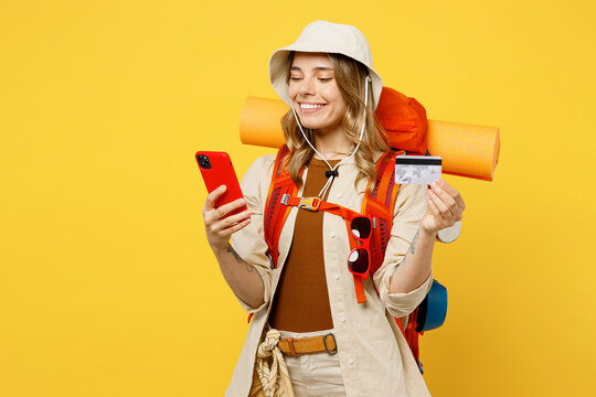 Young woman carry backpack with stuff mat use mobile cell phone credit card isolated on plain yellow background. Tourist leads active lifestyle walk on spare time Hiking trek rest travel trip concept