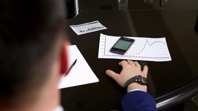 Businessman takes ringing cell phone in hand at meeting on blurred background backside view. Office manager checks call data crop body