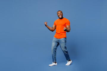 Full body young man of African American ethnicity he wears orange t-shirt doing winner gesture...