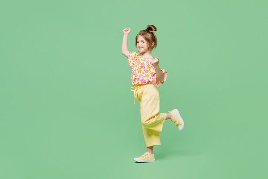 Full body little child kid girl 6-7 years old wear casual clothes doing winner gesture celebrate clenching fists say yes isolated on plain green background. Mother's Day love family lifestyle concept.
