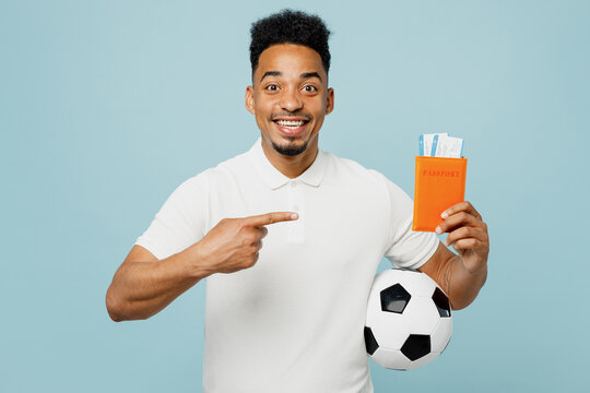 Traveler young man fan wear t-shirt cheer up support football sport team hold soccer ball show passport ticket isolated on plain blue background Tourist travel abroad. Air flight trip journey concept