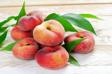 Fototapeta na wymiar Fresh Flat Peaches, Chinese Saturn Donut Peaches with Leaves on Wooden Bright Background