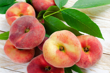 Fresh Flat Peaches, Chinese Saturn Donut Peaches with Leaves on Wooden Bright Background
