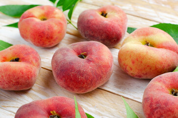 Fresh Flat Peaches, Chinese Saturn Donut Peaches with Leaves on Wooden Bright Background