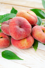 Naklejka na ściany i meble Fresh Flat Peaches, Chinese Saturn Donut Peaches with Leaves on Wooden Bright Background