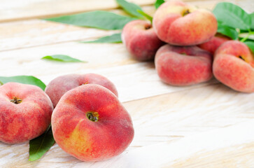 Naklejka na ściany i meble Fresh Flat Peaches, Chinese Saturn Donut Peaches with Leaves on Wooden Bright Background