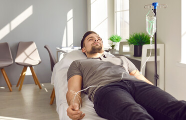 Obraz na płótnie Canvas Male patient receiving intravenous medication infusion at clinic. Young man lying on medical bed and getting medicine or vitamin solution through IV line. Therapy, treatment concept