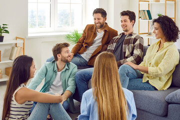 Group of a happy young friends men and women sitting in the living room at home talking with each other, laughing at joke enjoying meeting. Friendship, party and home leisure concept.