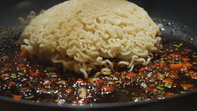 Dumping ramen noodles in sizzling sauté sauce