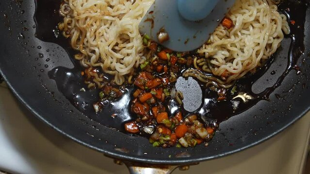 Stirring ramen noodles into the sauce in a pan on the stove in slow motion