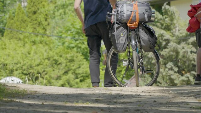 Male Standing Beside Touring Cycle With Pannier Bags Attached On Rear Wheel. Low Angle, Slow Motion