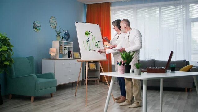 entertainment retired, elderly male and female painters paint a modern picture with brushes and paints on canvas in a cozy room