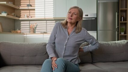 Unhappy mature caucasian woman feeling ache lower back pain on sofa at home unwell tired elderly female grandmother suffer from osteoarthritis arthritis lumbar spinal backache senior lady feel spasm