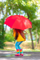 Happy beautiful girl with umbrella and color rubber boots jump on a rainy puddle