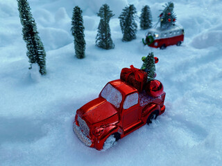 Christmas decorations in the form of red cars are carrying Christmas trees against the backdrop of snow. The concept of Christmas and winter holidays.