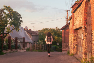 Modern woman riding her electric scooter on a village road