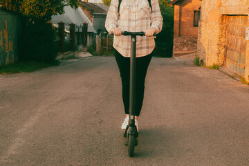 Modern girl riding her electric scooter on a village road covered with warm yellow sunset light. Back to school concept