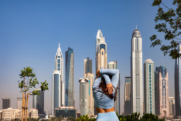 Rear view of sporty lady training exercise in urban park at Dubai skyscrapers backdrop. From behind...