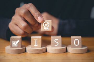 Wooden cube with a guarantee icon and smart globe ISO icons, symbolizing quality control certification. Hand flipping the ISO icons shows compliance with international standards.