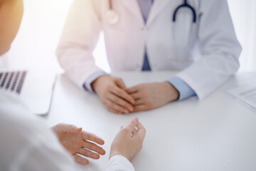 Doctor and patient discussing current health questions while sitting opposite of each other at the table in clinic, just hands closeup. Medicine concept