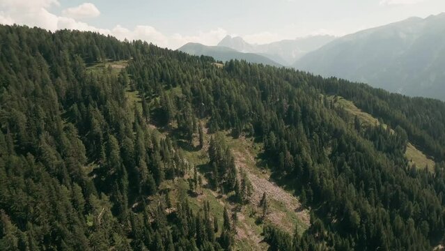 FPV drone navigates through a lush forest, revealing the awe-inspiring grandeur of the Dolomite mountains in captivating footage of the breathtaking beauty of Luzen village from an aerial perspective.