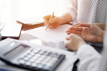 Woman accountant using a calculator and laptop computer while counting taxes for a client. Business...