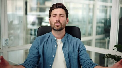 Calm mindful young businessman taking break sit at office place meditating doing exercise feel no stress free relief relaxing, healthy serene guy practicing yoga breathing for peaceful mind and zen.