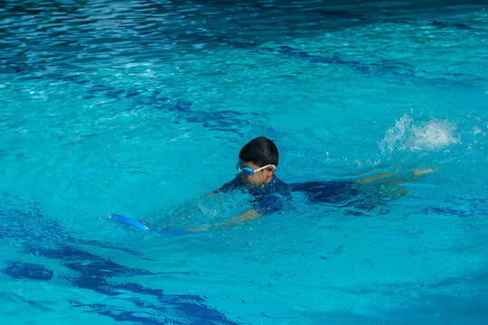 Image of lonely Asian young boy age 6-7 years old hold a kickboard to learning to use the legs for beginner swimming on butterfly position. Background for recreation or outdoor sport concept.