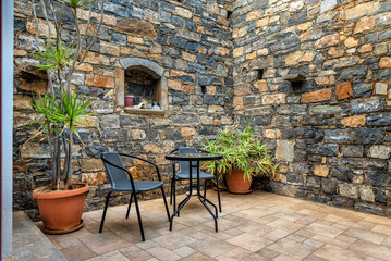 Backyard of the stone house with table and two chairs and outdoor flower pots.