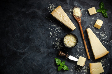 Set of hard cheeses with cheese knives on black stone background. Parmesan. Top view. Free space...