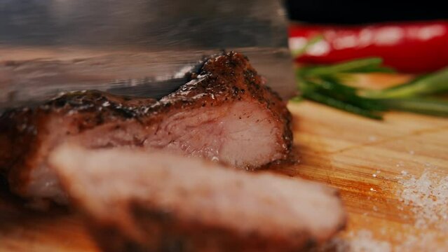 Close-up slicing delicious juicy steak on cutting board with kitchen axe. Closeup cutting tasty meat in slow motion
