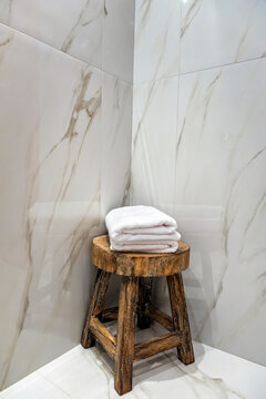 Bathroom detail. Wooden stool in the corner with folded towels on it. Marble like tiled walls.