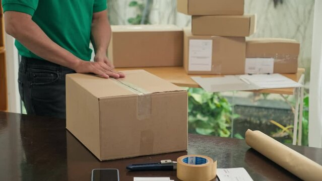 Cropped shot of delivery worker holding and sealing cardboard box with sticky tape at office