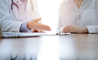 Doctor and patient discussing something while sitting near each other at the wooden desk in clinic. Medicine concept