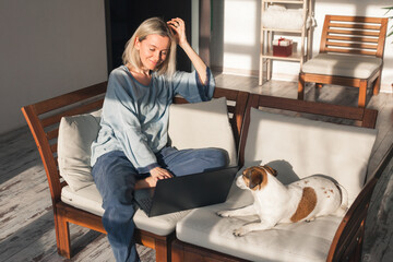 Happy middle aged woman with dog using her laptop at cozy white home