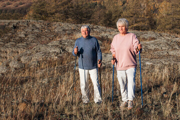 Happy middle age woman and man walking with Scandinavian sticks in autumn forest