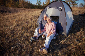 Naklejka na ściany i meble Camping tent vacation Senior couple man and woman sitting near camp tent